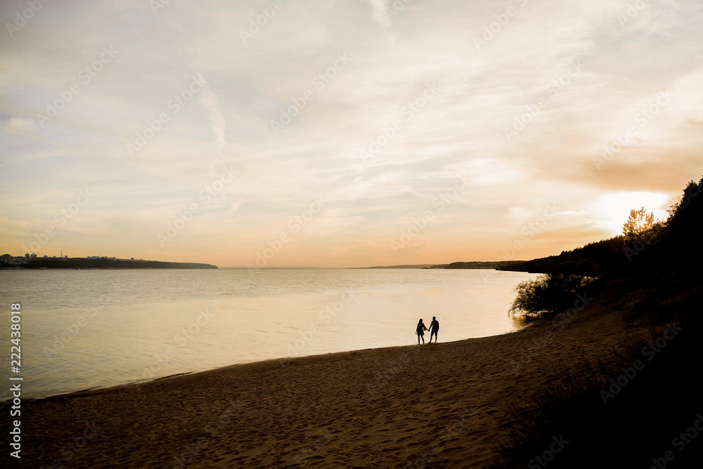 Two lovers stroll along the river at sunset.