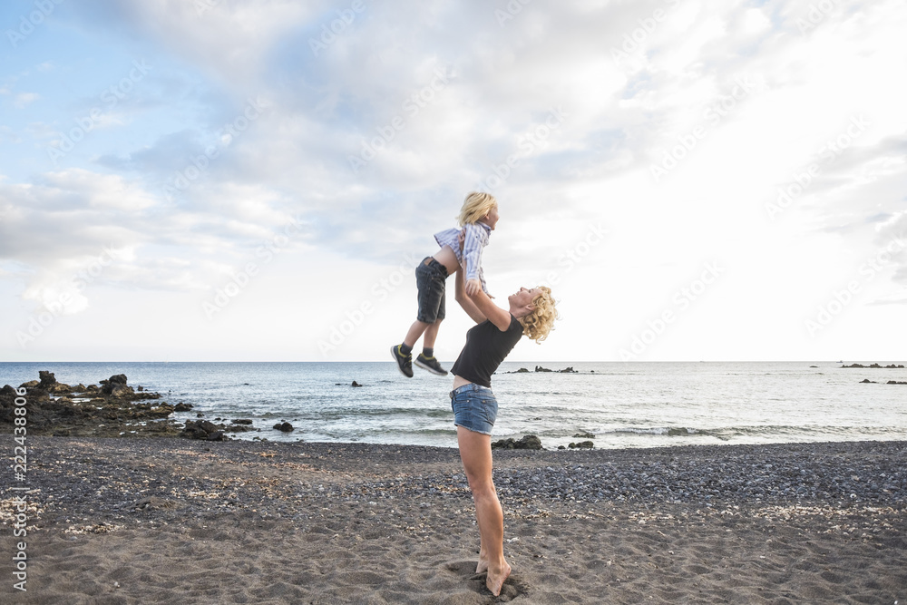 joyful happiness concept  love between caucasian woman and little boy mother and son hugging and playing in vacation leisure activty with sunset and clouds in background. lifestyle for happy people