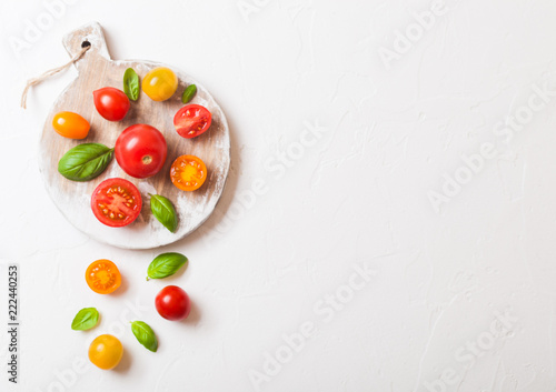 Organic Mini Tomatoes with basil and pepper on chopping board on stone kitchen background. San Marzano, orange and plum tomatoes