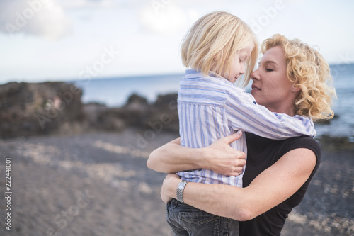 young beautiful blonde eas europe mother woman kiss her son while hug him with love and togetherness emotion and feeling. enjoy life and lifestyle for nice family outdoor - single mom