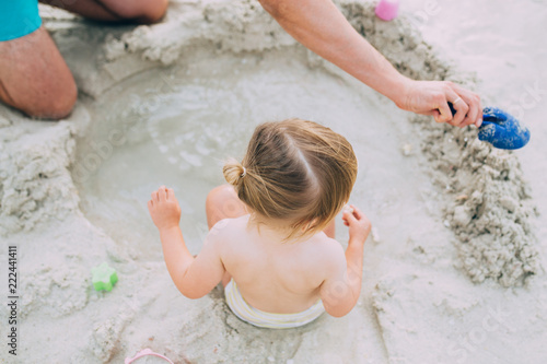 Adorable baby girl and her father playing with sand on beach