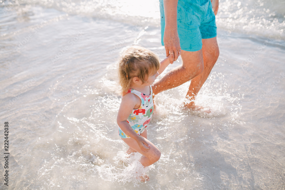 Adorable baby girl and her father playing with sand on beach Adorable baby girl and her father playing with sand on beach