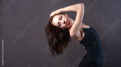 Elegant ballerina posing in a trough on a brown background, the model has eyes closed and long dark hair. Studio photography.