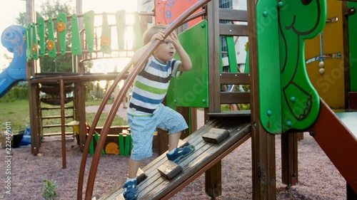 4k video of funny toddler boy climbing on wooden stapladder on children playground at park photo