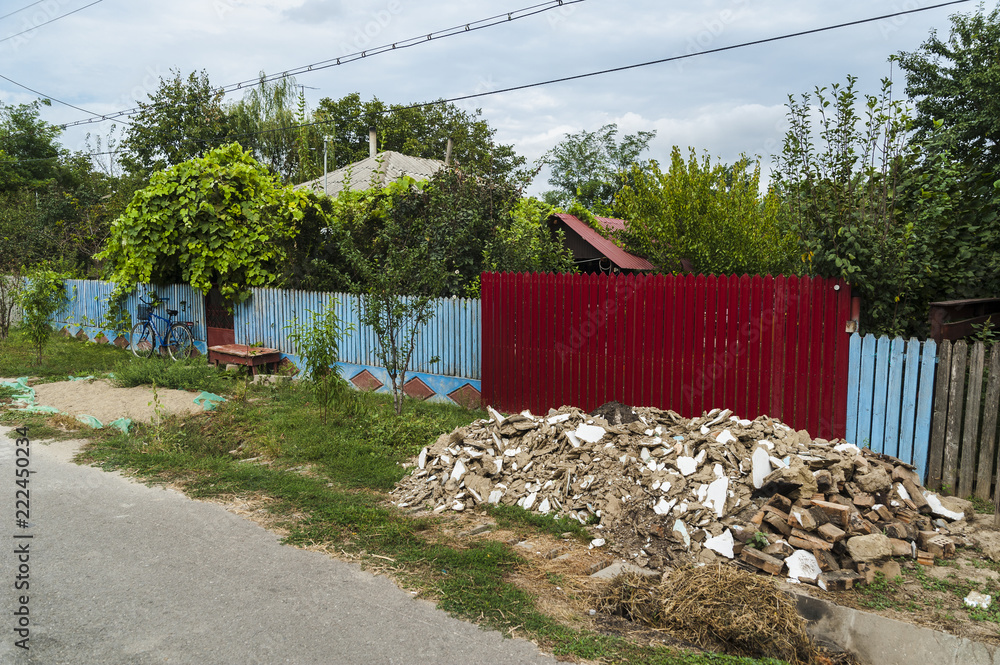 Φωτογραφία Bright colored fences/Romanian village street with colored wooden fences, a pile of debris and a bike leaning on a blue fence