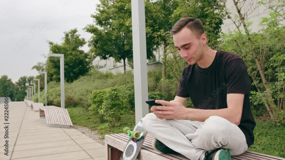 A young man using a phone sitting on the pavement in town. Medium shot. Soft focus A young man using a phone sitting on the pavement in town. Medium shot. Soft focus