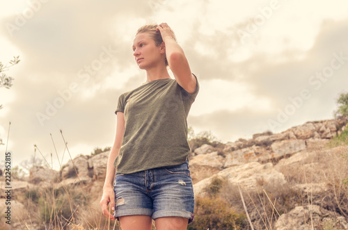 A lost woman stands against the background of a rocky mountain and a gray sky