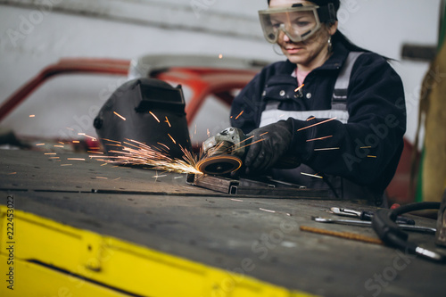 Strong and worthy woman doing hard job in car and motorcycle repair shop. She using grinder to fix some metal bike parts. photo