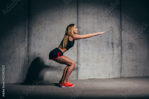 Fit young woman doing squats during urban workout session