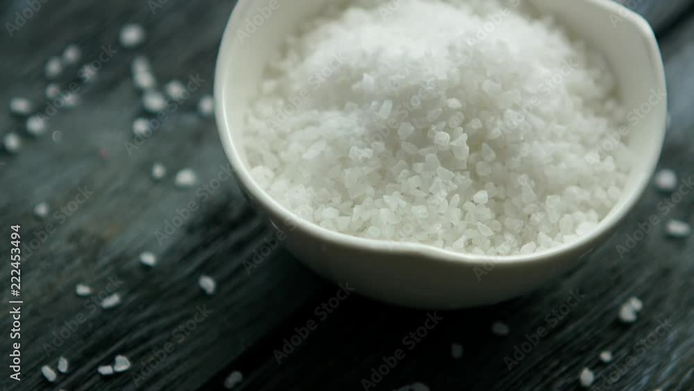 From above white salt in a bowl placed on dark wooden table From above white salt in a bowl placed on dark wooden table