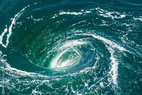 High angle view of a powerful whirlpool at the surface of green water with foam.