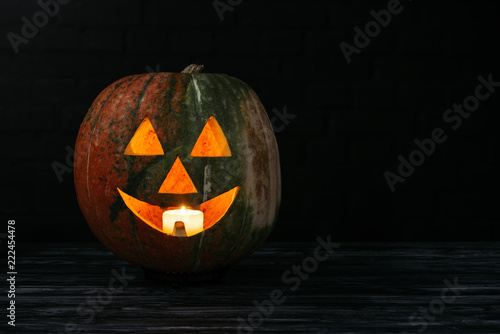 jack o lantern pumpkin with candle inside on wooden table on black background