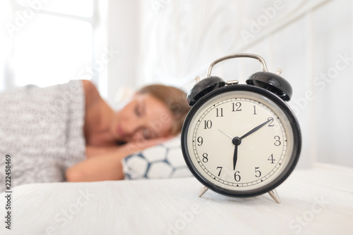 Analog alarm clock. Woman sleeping in bed