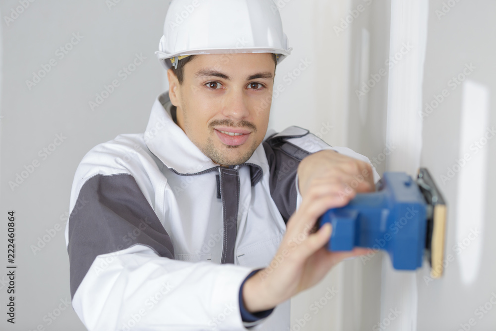 young builder in hardhat sanding wall indoors young builder in hardhat sanding wall indoors