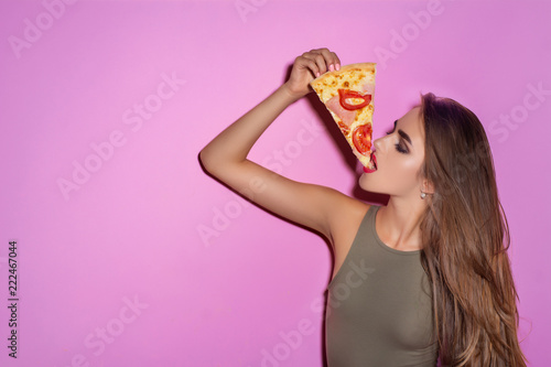 One pretty young sexy woman with long hair and bright makeup holding tasty big slice of pizza ready to eat standing in studio on pink background. Girl eating a delicious pizza