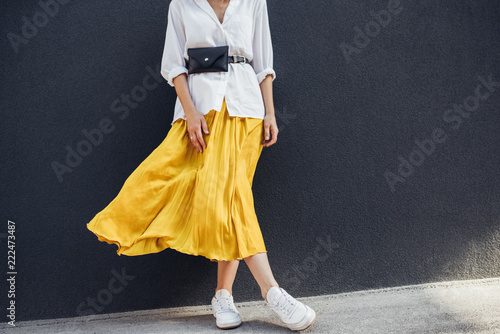Horizontal cropped body image of beautiful slim woman in beautiful yellow skirt. Caucasian female fashion model standing over gray wall background outdoor with copy space.