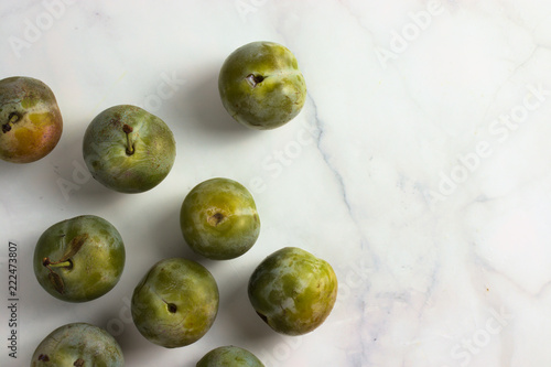 Group of small greengage plums on white marble, top view, copy space photo