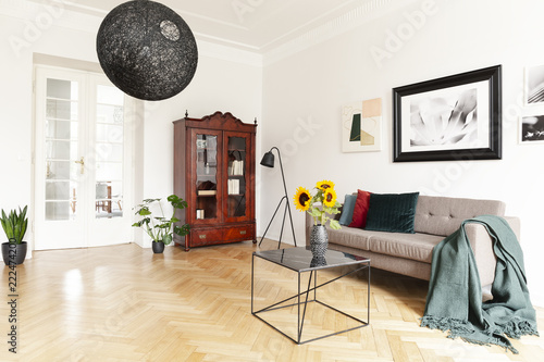 A dark, wooden, display cabinet by a white wall of an eclectic living room interior with yellow sunflowers and art photo
