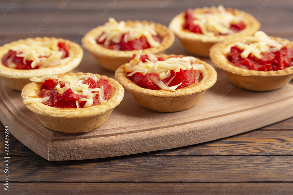 Mini pizza with salami, tomato and cheese on wooden background. Tasty appetizer, tartlet. Mini pizza with salami, tomato and cheese on wooden background. Tasty appetizer, tartlet.
