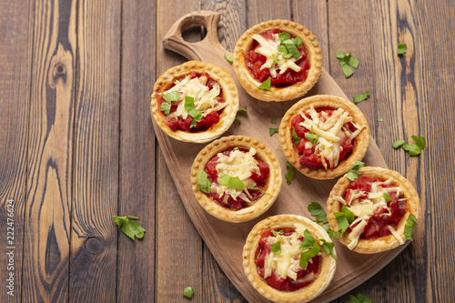 Mini pizza with salami, tomato and cheese on wooden background. Tasty appetizer, tartlet.