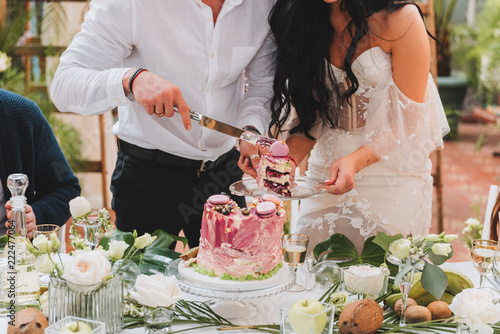 Gorgeous bride and groom cutting a small modern wedding cake on a table with various decorations