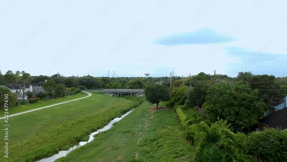 Aerial scene moving down over large detention pond and drainage canal that is part of flood control for large suburban area with biking trail running adjacent and a bridge crossing in the distance. Aerial scene moving down over large detention pond and drainage canal that is part of flood control for large suburban area with biking trail running adjacent and a bridge crossing in the distance.