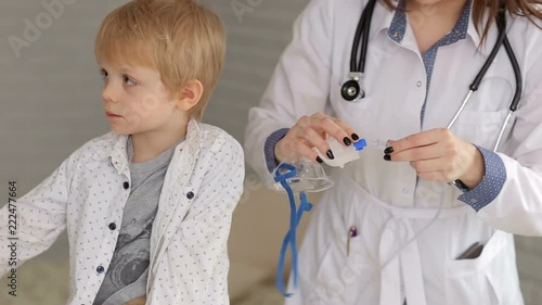 Cute little boy making inhalation with a nebulizer mask in the hospital. Kid allergy concept. Portrait of a woman pediatrician and a little boy with an inhalation mask from a nebulizer in the hospital photo