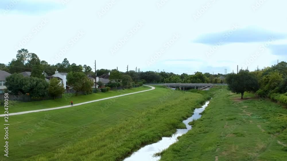 Aerial dolly of a large retention pond and drainage canal that is part of flood control for a large suburban area with a person walking on the biking trail that runs adjacent to it. Aerial dolly of a large retention pond and drainage canal that is part of flood control for a large suburban area with a person walking on the biking trail that runs adjacent to it.