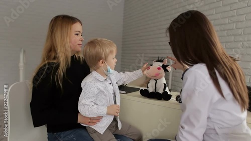 Female pediatrician talking to young child and mother on inspection in the clinic. Mother and son visiting pediatrician. The doctor plays with the baby and with the toy. photo