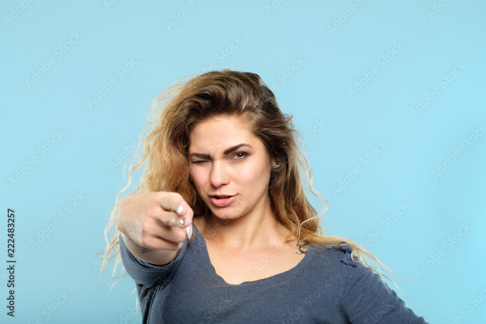 confident beautiful seductive woman pointing a finger gun at you. femme fatale aiming for your heart. alluring and provocative portrait of a girl on blue background.