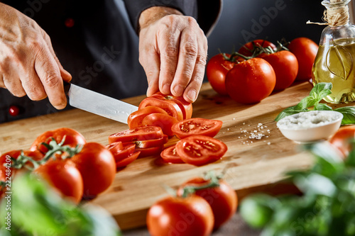 Chef slicing fresh ripe tomatoes on a board