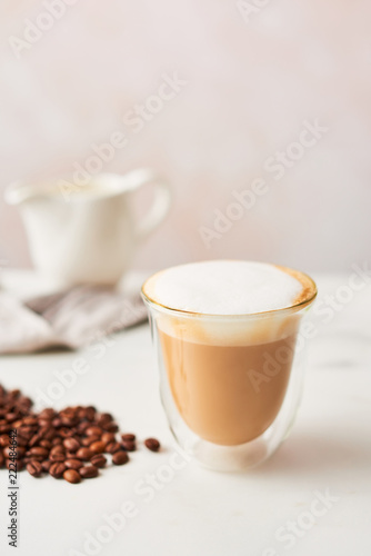 Cappuccino in a double walled glass with roasted coffee beans. Feminine rose background with copy space. High resolution image, narrow depth of field.