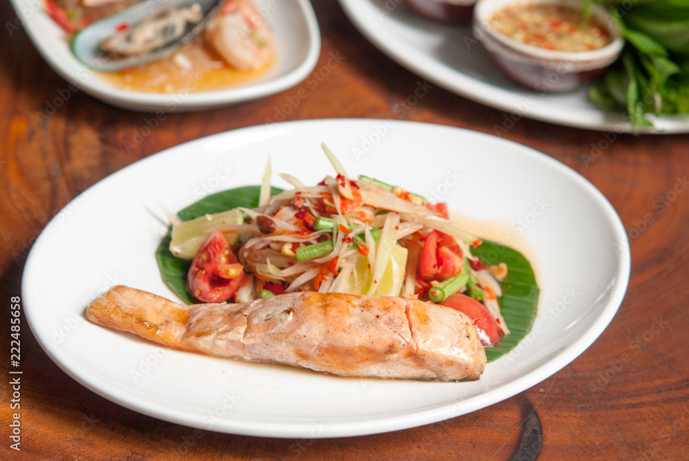 Grilled salmon steak, spicy Thai papaya salad  in white dish on wooden table background