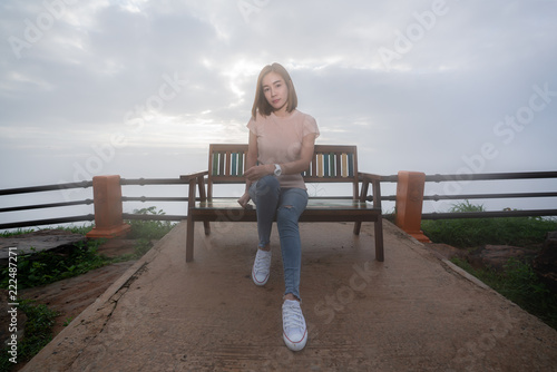 Beautiful asian woman in casual sitting on bench behind a beautiful sunset pass through sky clouds © KissShot