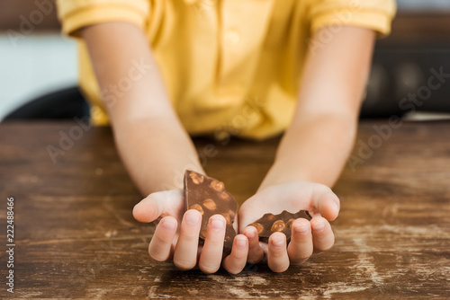 close-up partial view of child holding pieces of delicious chocolate with hazelnuts