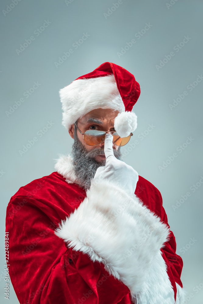 Funny serious guy with christmas hat posing at studio. New Year Holiday. Christmas, x-mas, winter, gifts concept. Man wearing Santa Claus costume on gray. Copy space. Winter sales. Funny serious guy with christmas hat posing at studio. New Year Holiday. Christmas, x-mas, winter, gifts concept. Man wearing Santa Claus costume on gray. Copy space. Winter sales.