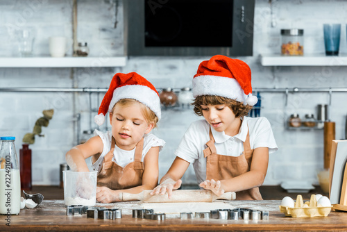 adorable chldren in santa hats and aprons preparing christmas cookies together photo