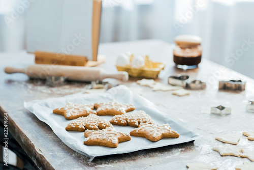 close-up view of delicious ginger cookies on baking tray, cookbook and ingredients on table