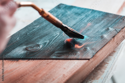Foto Artisan and carpenter burning wood planks, focus on the gas burner pistol, made of brass and orange rubber cable