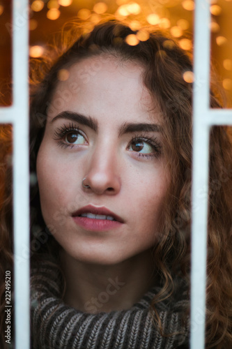 Warm, wintery portrait of young adult, female, gazing out the window with drops of water and bokeh