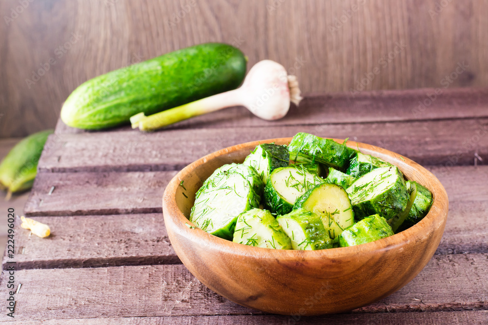 Freshly salted cucumber pickled with garlic and dill in a wooden plate Freshly salted cucumber pickled with garlic and dill in a wooden plate