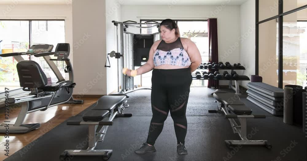 Overweight woman doing workout with dumbbell at gym or fitness center Overweight woman doing workout with dumbbell at gym or fitness center