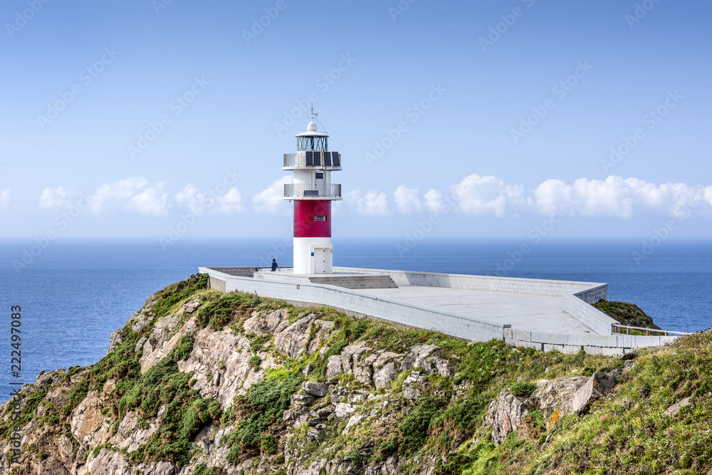 Spain, Cabo Ortegal: Seascape with beautiful red white striped lighthouse, people tourists, coastline, ocean sea water, cliff, skyline and blue sky in background - concept navigation. July 13, 2018
