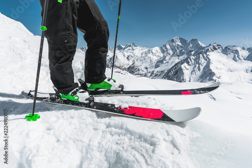 A close-up of the ski on the athlete's feet against the background of snow-capped rocky mountains. The concept of winter sports in the mountains