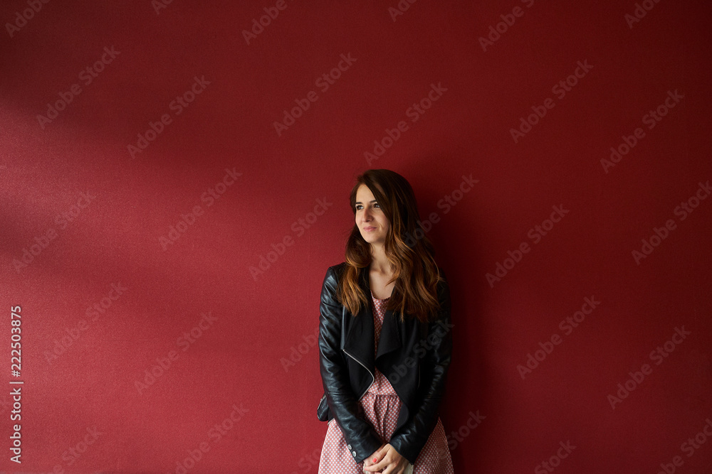 Young woman in jacket standing near red wall Young woman in jacket standing near red wall