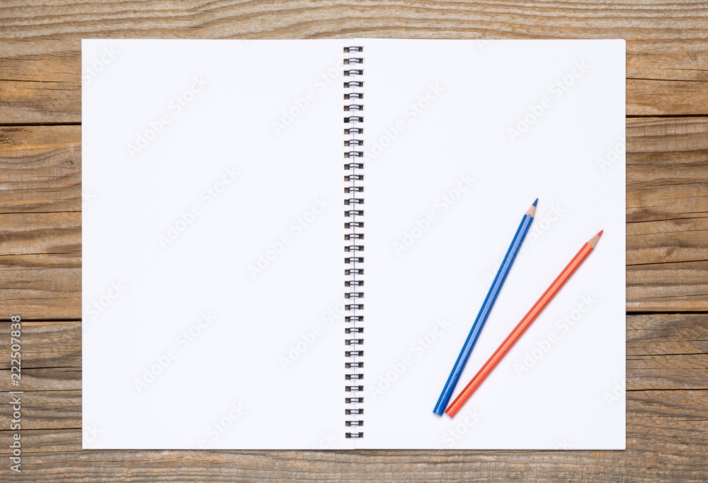 Blank page of a sketchbook with colored pencils on an old wooden table Blank page of a sketchbook with colored pencils on an old wooden table
