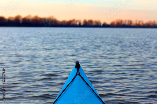 View from the blue kayak on the river banks in fall season. Bow of blue kayak on Danube river. Kayaking on peaceful calm lake or river at sunny autumn evening