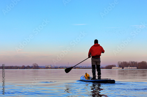 Man rowing with a paddle on the stand up paddle board  paddleboard  SUP  in the Danube river at calm cold winter day