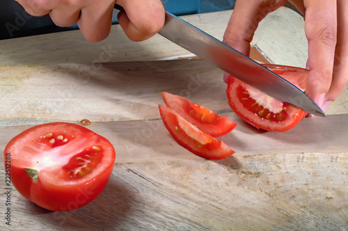 Female hands with knife, cutting fresh red tomatoes.