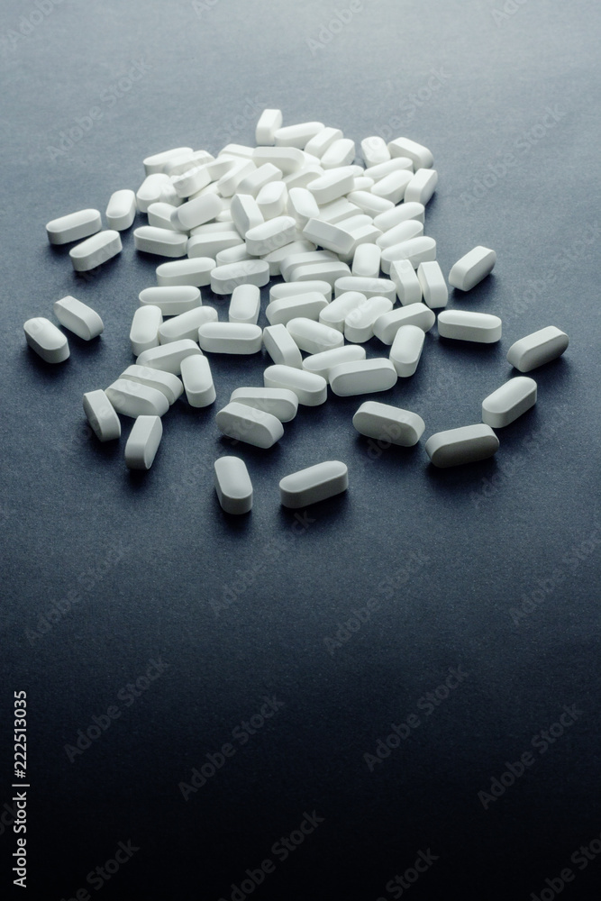 A bunch of white tablet pills (medications or drugs) on a flat surface. Dark ominous lighting, vertical shot.
A bunch of white tablet pills (medications or drugs) on a flat surface. Dark ominous lighting, vertical shot.